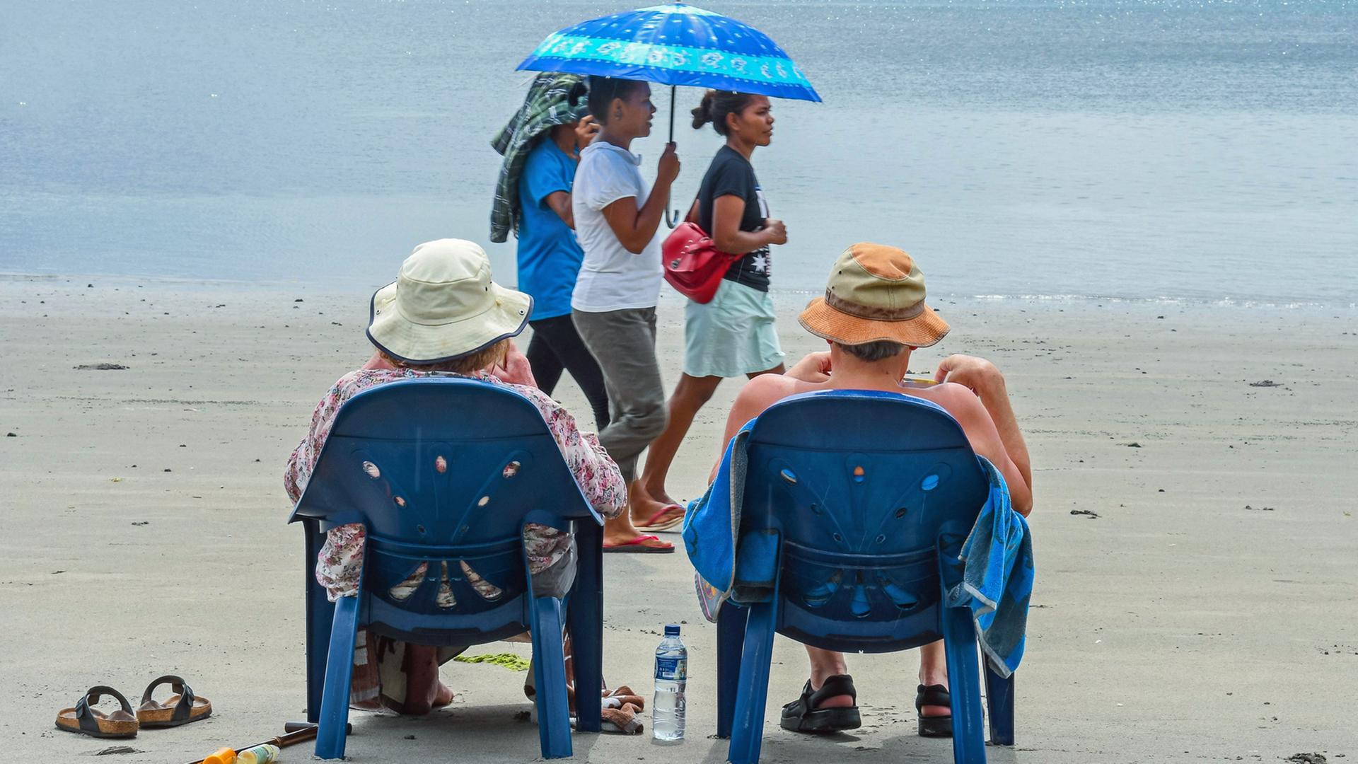 Touristen mit Sonnenhut sitzen in Stühlen am Strand in Atauro. Touristen mit Sonnenhut sitzen in Stühlen am Strand in Atauro.