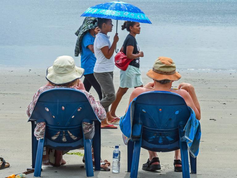 Touristen mit Sonnenhut sitzen in Stühlen am Strand in Atauro.