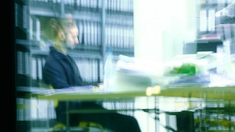 Ein Mann sitzt abends in einem Büro an einem vollen Schreibtisch und arbeitet in Berlin. Ein Mann sitzt abends in einem Büro an einem vollen Schreibtisch und arbeitet in Berlin.