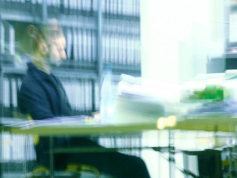 Ein Mann sitzt abends in einem Büro an einem vollen Schreibtisch und arbeitet in Berlin.