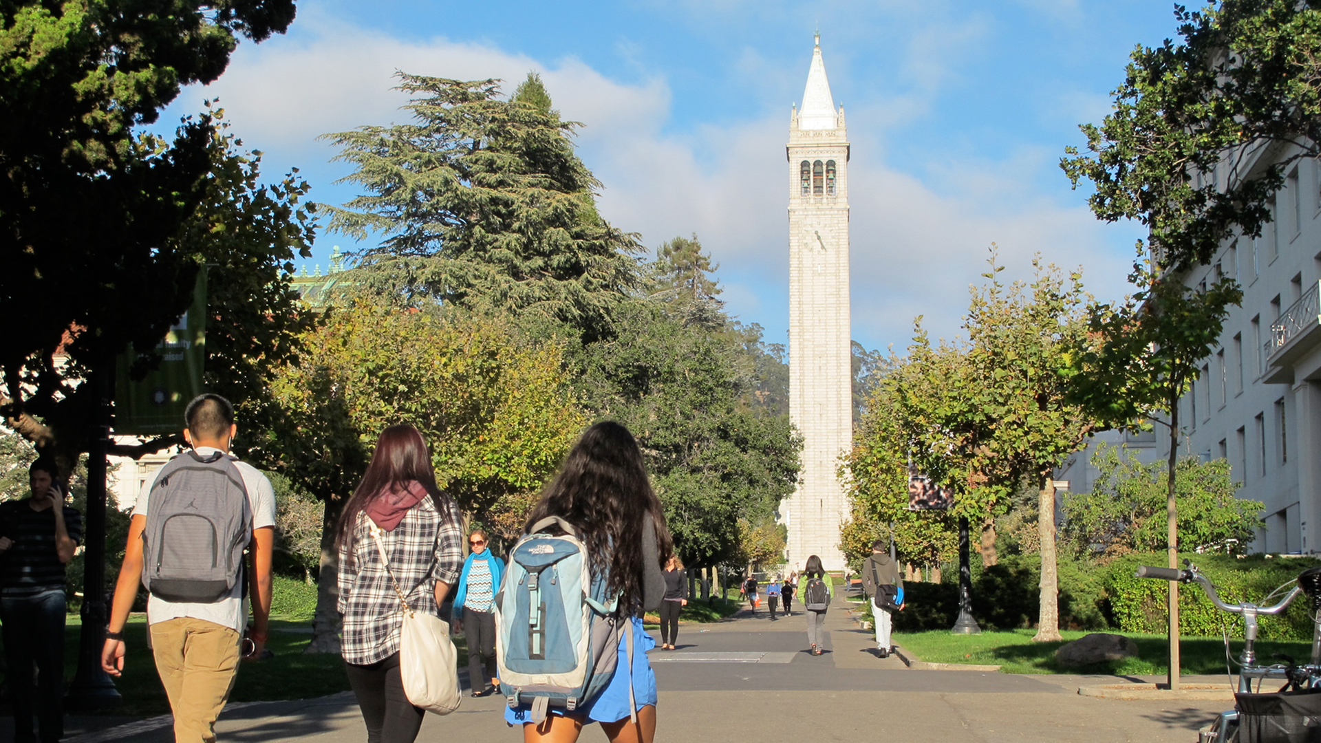 Studenten gehen über den Campus der Universität in Berkeley mit dem Campanile, einem Glockenturm und Wahrzeichen des Gebäudes.
