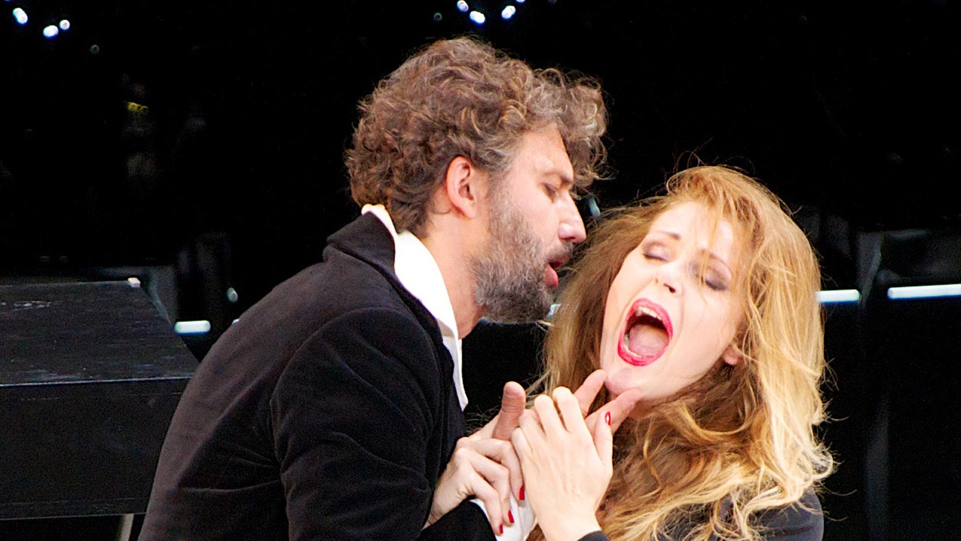 Jonas Kaufmann und Kristine Opolais singend in halber Umarmung. Jonas Kaufmann und Kristine Opolais singend in halber Umarmung.