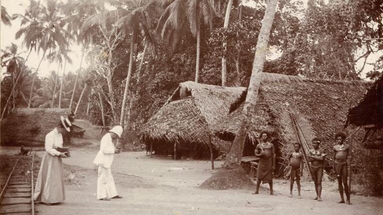 Historisches Foto: Eine weiße Frau mit Hut und langem Rock und ein weißer Mann im Tropenanzug - Marion und Albert Dommes fotografieren Einwohner des Dorfes Bogadjim auf Papua-Neuguinea. Die Namen der Einwohner sowie des Fotografen sind nicht überliefert. Originaltitel: "Dorf bei Stephansort". Rautenstrauch-Joest-Museum – Kulturen der Welt, Fotografische Sammlung, Inv. Nr. 9240 Historisches Foto: Eine weiße Frau mit Hut und langem Rock und ein weißer Mann im Tropenanzug - Marion und Albert Dommes fotografieren Einwohner des Dorfes Bogadjim auf Papua-Neuguinea. Die Namen der Einwohner sowie des Fotografen sind nicht überliefert. Originaltitel: "Dorf bei Stephansort". Rautenstrauch-Joest-Museum – Kulturen der Welt, Fotografische Sammlung, Inv. Nr. 9240