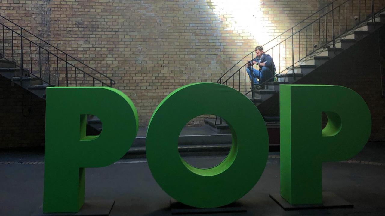 Mann sitzt auf Treppe und wird von einem Lichtschein erhellt. Im Vordergrund steht in großen grünen Buchstaben das Thema der aktuellen re:publica: “Pop” Mann sitzt auf Treppe und wird von einem Lichtschein erhellt. Im Vordergrund steht in großen grünen Buchstaben das Thema der aktuellen re:publica: “Pop”