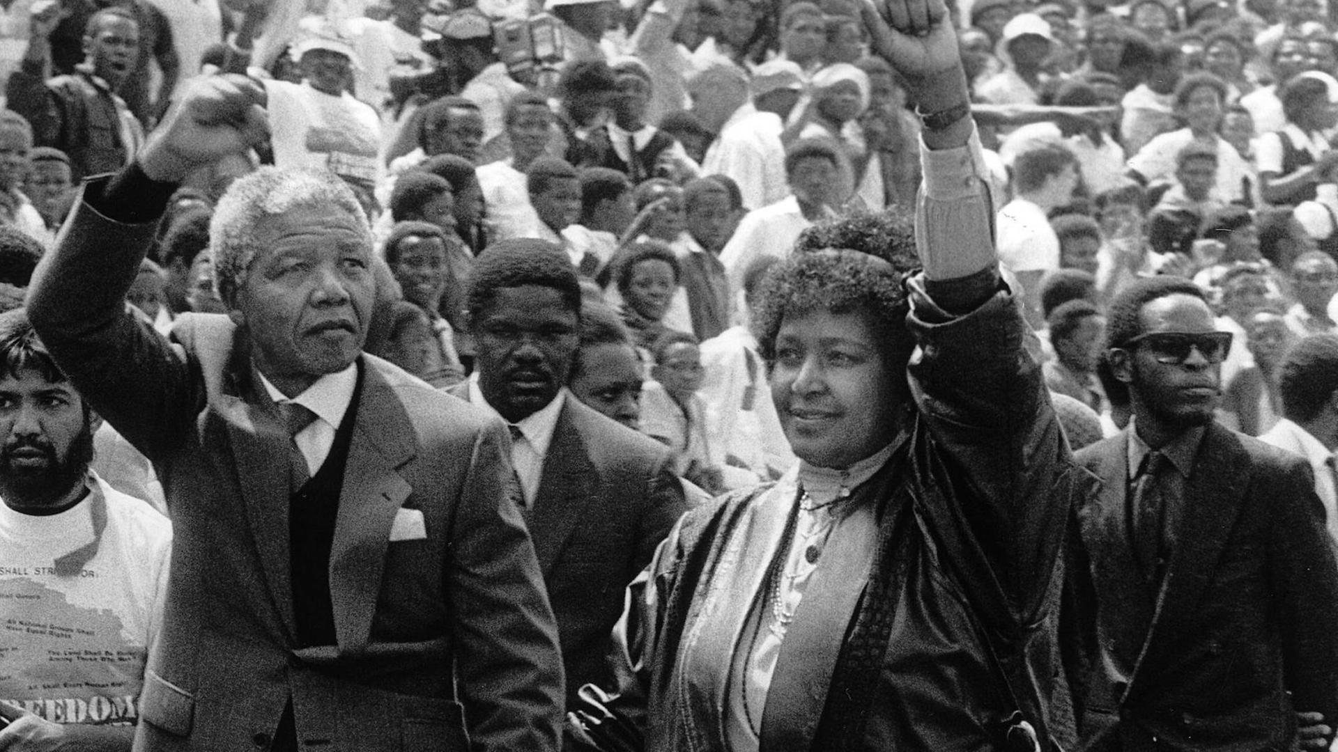 Nelson Mandela und seine Frau Winnie laufen durch eine Menschenmenge und heben ihre Fäuste.