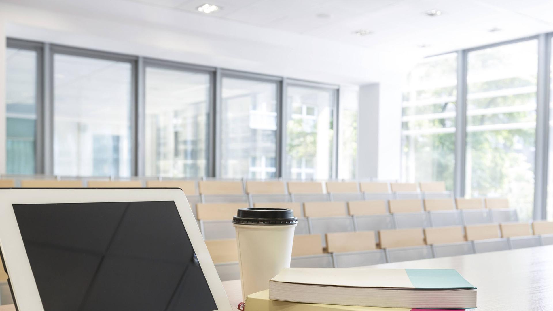 Ein Unterrichtsraum mit einem Tisch auf dem ein Tablet mit Lernbüchern und einer Kaffeetasse steht. Ein Unterrichtsraum mit einem Tisch auf dem ein Tablet mit Lernbüchern und einer Kaffeetasse steht.