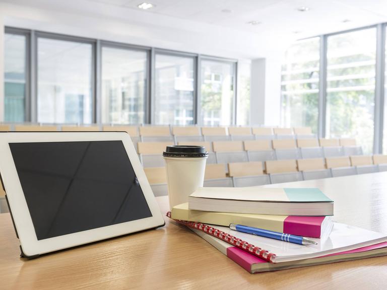 Ein Unterrichtsraum mit einem Tisch auf dem ein Tablet mit Lernbüchern und einer Kaffeetasse steht. 