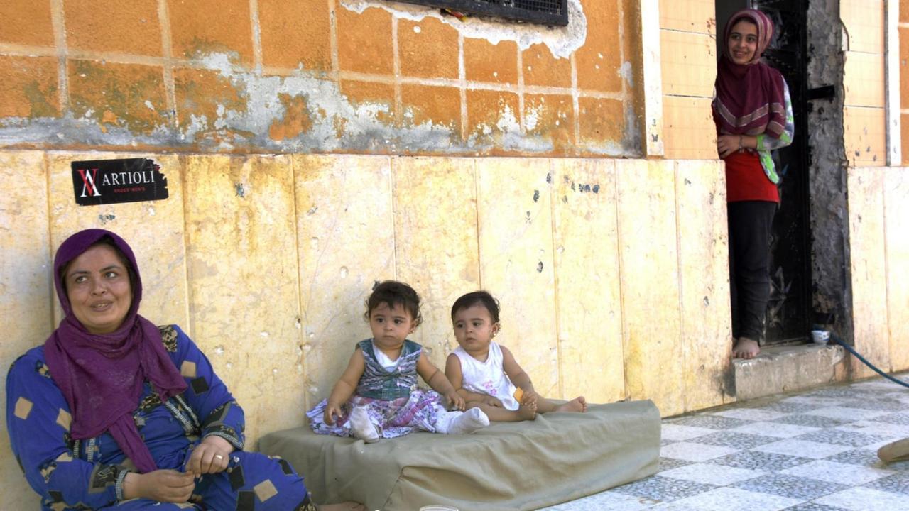 Eine Frau und zwei Kinder sitzen vor ihrem Haus in Aleppo. In der Hauswand sieht man viele Einschusslöcher. Eine Frau und zwei Kinder sitzen vor ihrem Haus in Aleppo. In der Hauswand sieht man viele Einschusslöcher.