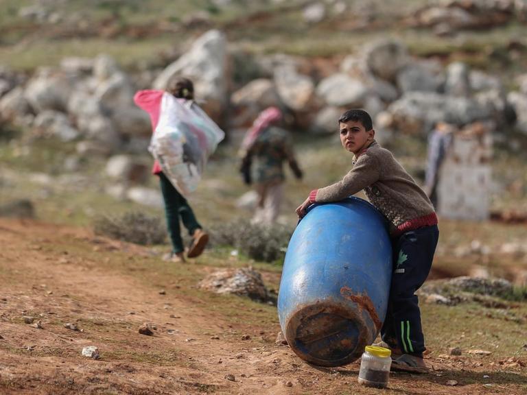 Ein syrischer Junge hält ein Plastikfass, im Hintergrund laufen Kinder mit Plastiksäcken.