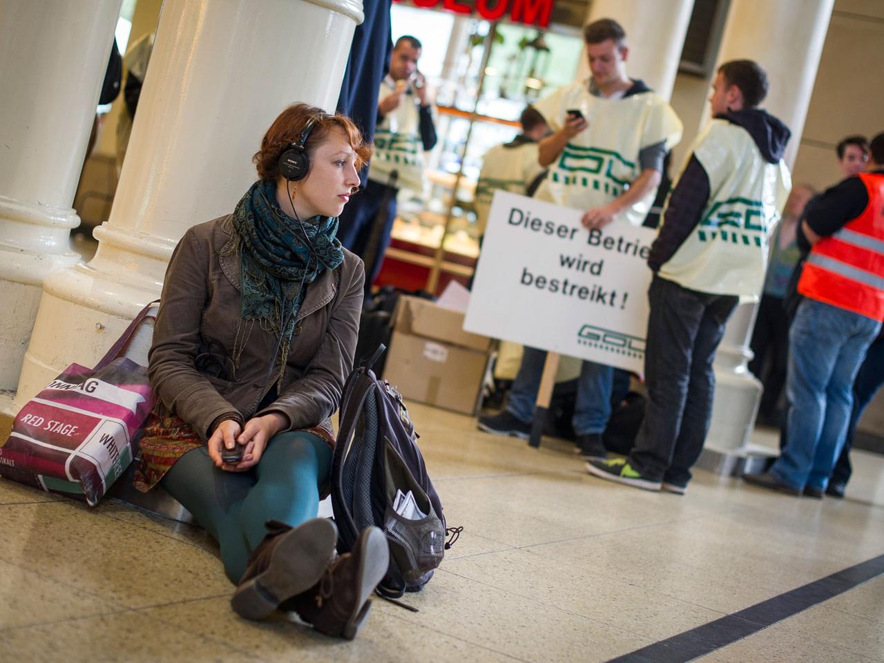 Eine junge Frau mit Kopfhörern wartet am 15.10.2014 im Hauptbahnhof Hannover (Niedersachsen) sitzend auf einen Zug, während im Hintergrund Lokführer stehen. Eine junge Frau mit Kopfhörern wartet am 15.10.2014 im Hauptbahnhof Hannover (Niedersachsen) sitzend auf einen Zug, während im Hintergrund Lokführer stehen.