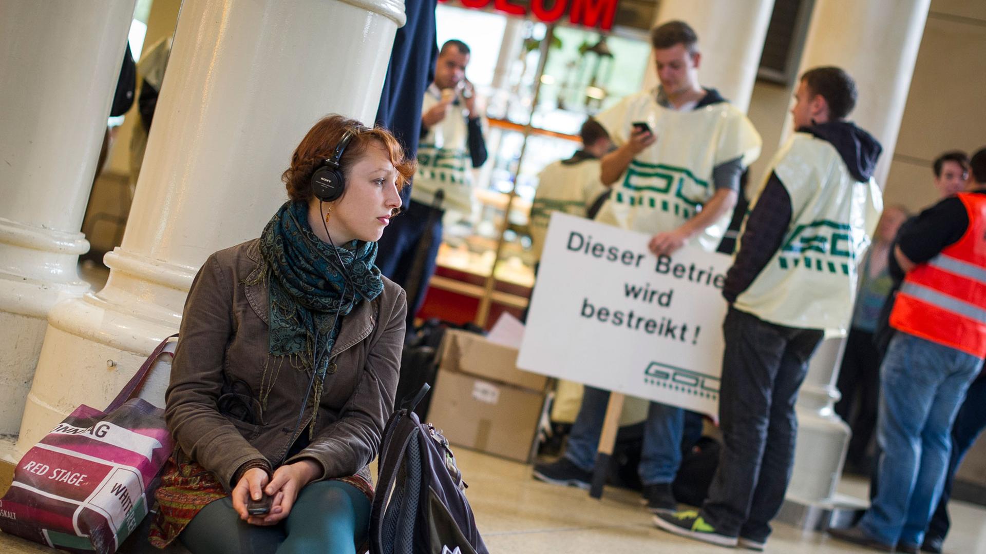 Eine junge Frau mit Kopfhörern wartet am 15.10.2014 im Hauptbahnhof Hannover (Niedersachsen) sitzend auf einen Zug, während im Hintergrund Lokführer stehen. Eine junge Frau mit Kopfhörern wartet am 15.10.2014 im Hauptbahnhof Hannover (Niedersachsen) sitzend auf einen Zug, während im Hintergrund Lokführer stehen.