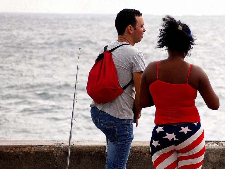 Ein Paar steht an einer Mauer und schaut auf das Meer.