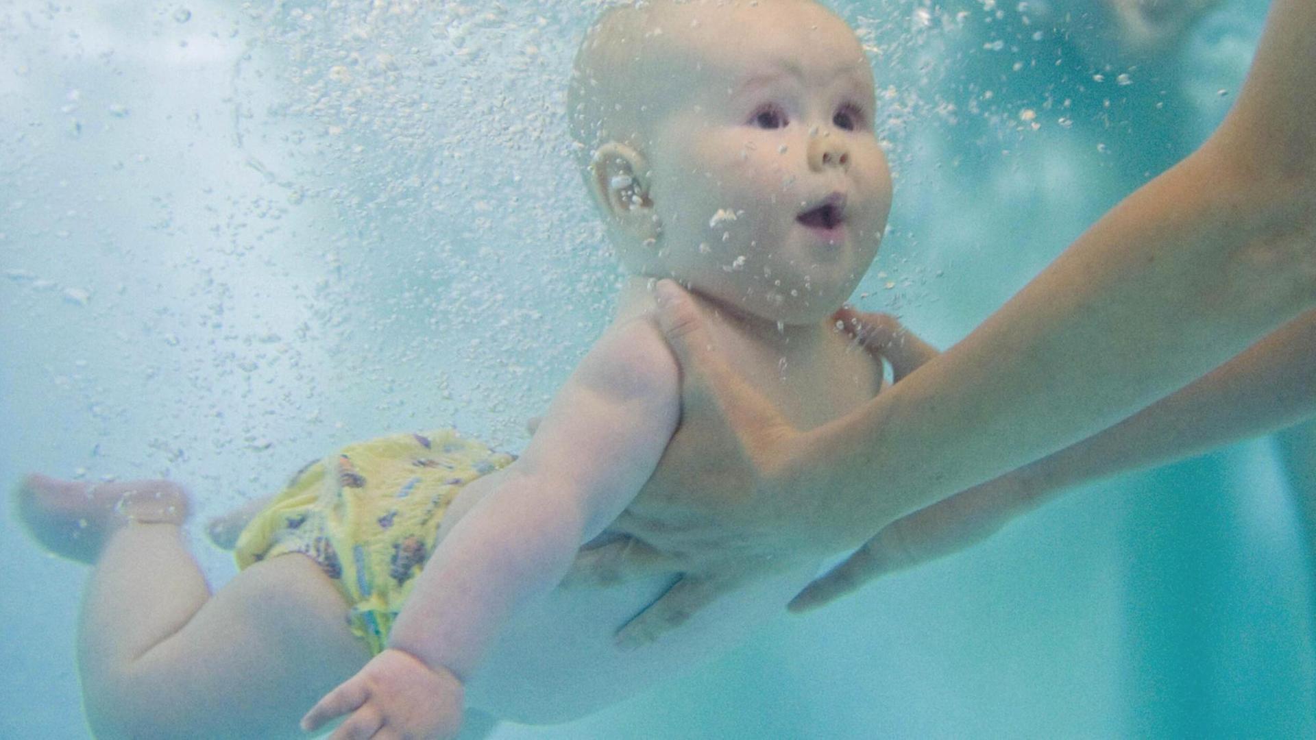 Die Unterwasseraufnahme eines Babys, das beim Schwimmunterricht unter Wasser festgehalten wird Die Unterwasseraufnahme eines Babys, das beim Schwimmunterricht unter Wasser festgehalten wird