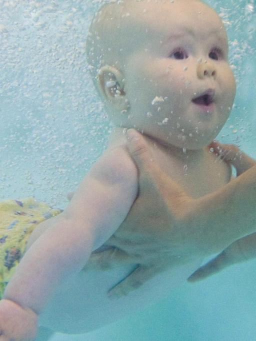 Die Unterwasseraufnahme eines Babys, das beim Schwimmunterricht unter Wasser festgehalten wird
