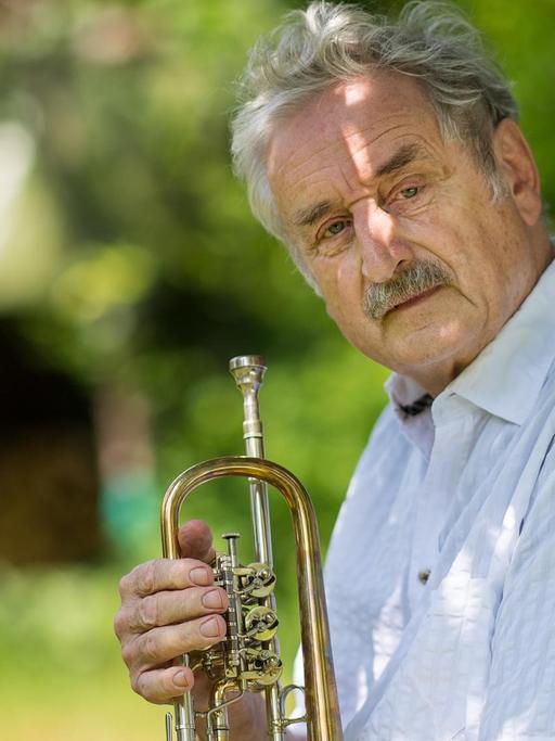 Der Trompeter Ludwig Güttler sitzt in seinem Garten und hält eine Trompete in der Hand.