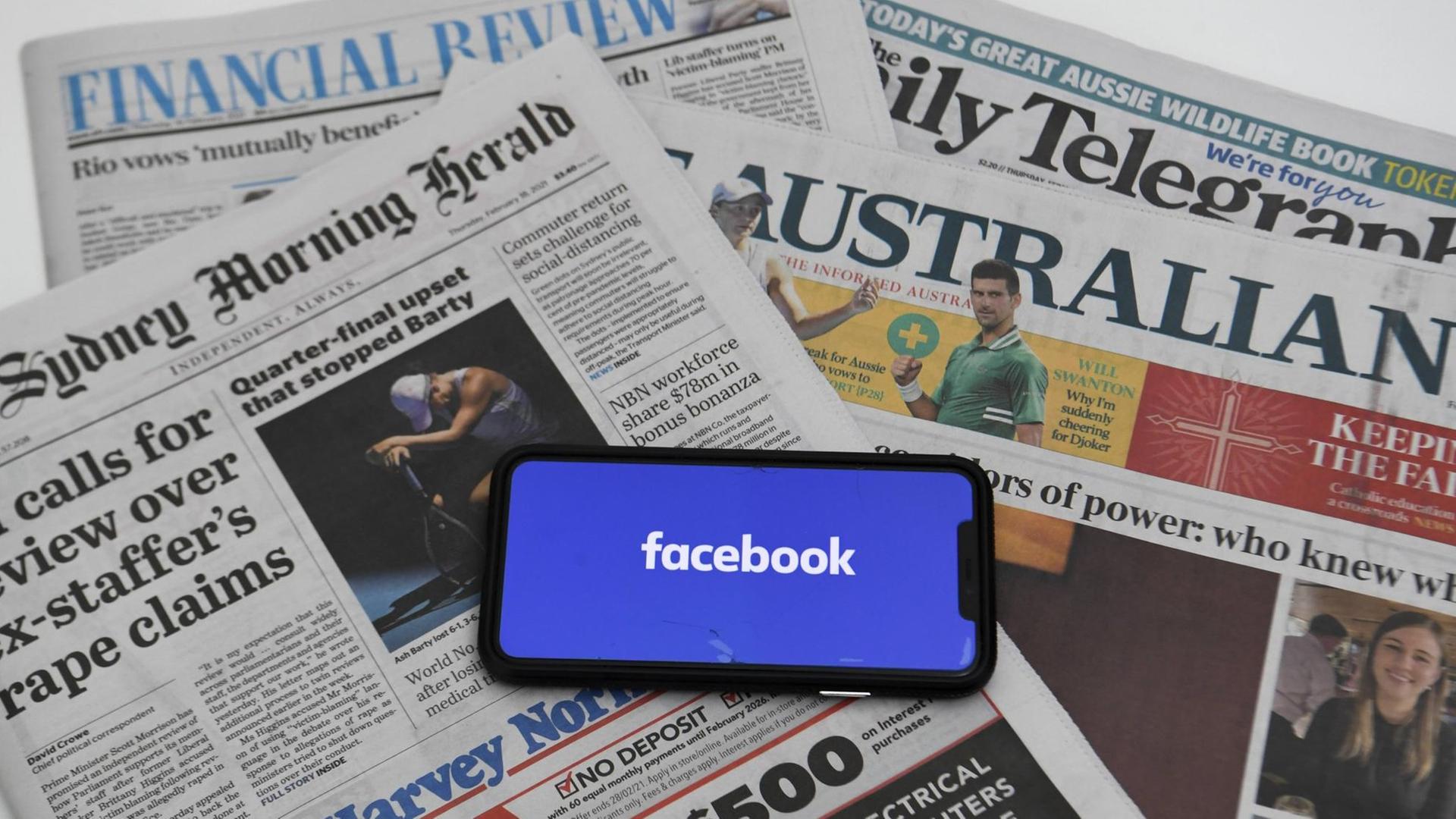 Auf mehreren australischen Tageszeitungen liegt ein Smartphone, das das Facebook-Logo zeigt Auf mehreren australischen Tageszeitungen liegt ein Smartphone, das das Facebook-Logo zeigt
