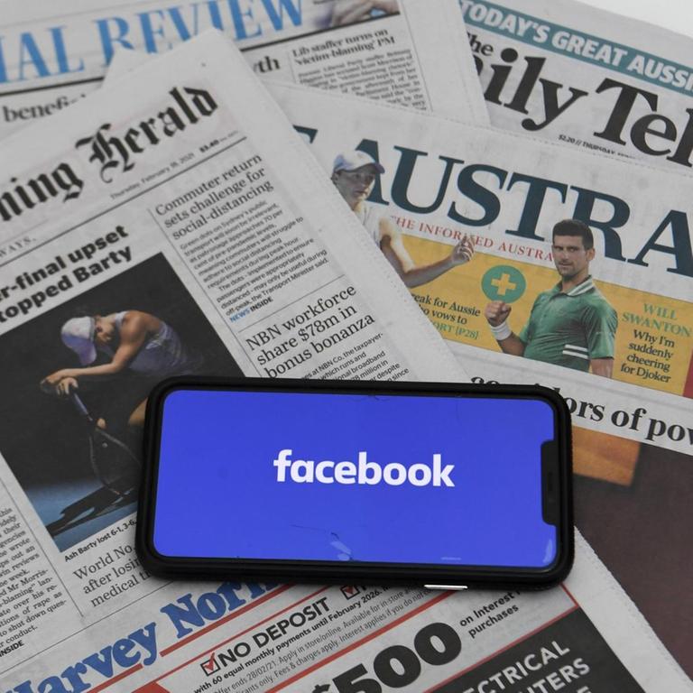 Auf mehreren australischen Tageszeitungen liegt ein Smartphone, das das Facebook-Logo zeigt