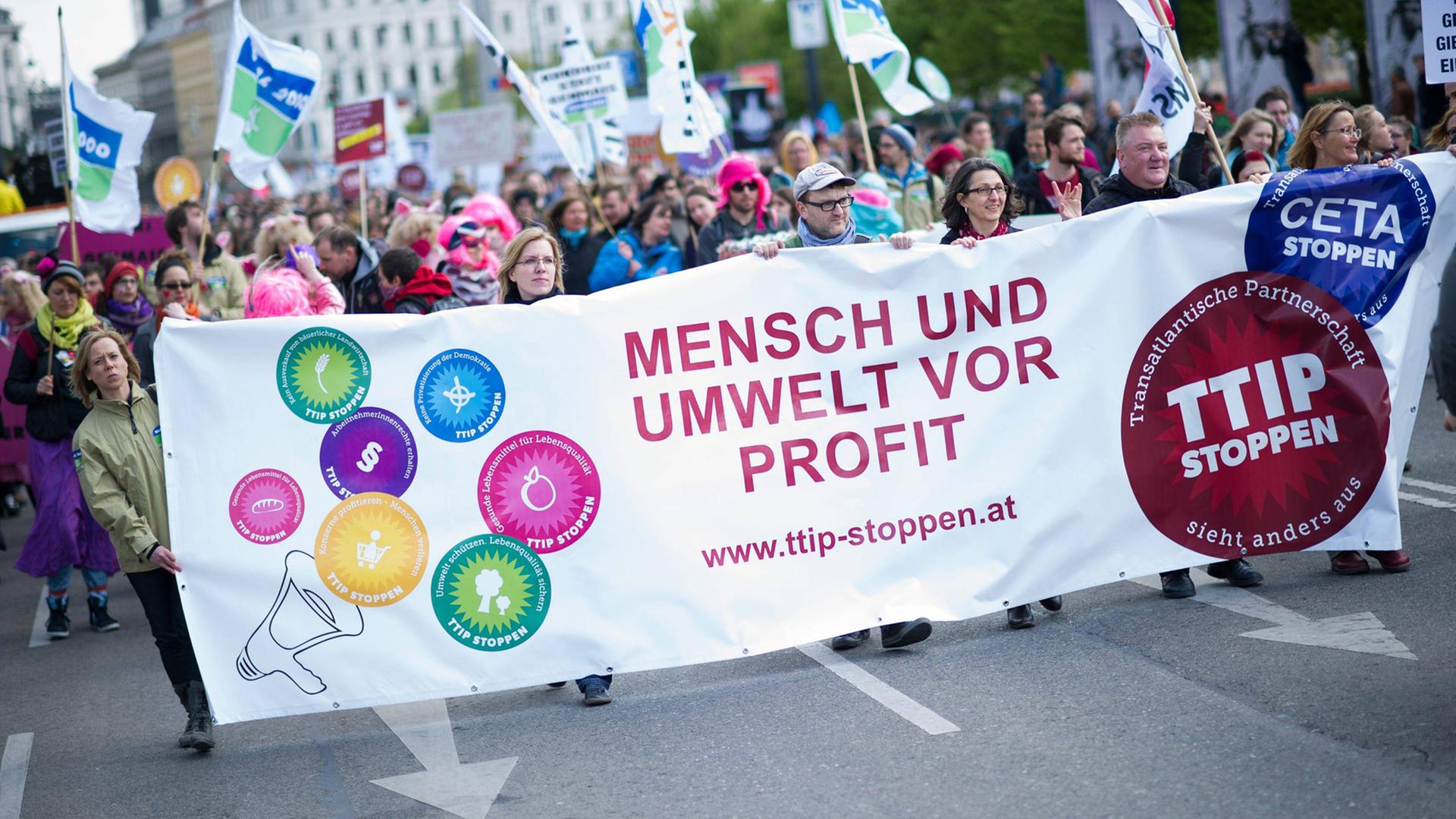 Menschen demonstrieren in Wien gegen das TTIP-Abkommen. Sie halten ein Transparent mit der Aufschrift "Mensch und Umwelt vor Profit". Menschen demonstrieren in Wien gegen das TTIP-Abkommen. Sie halten ein Transparent mit der Aufschrift "Mensch und Umwelt vor Profit".
