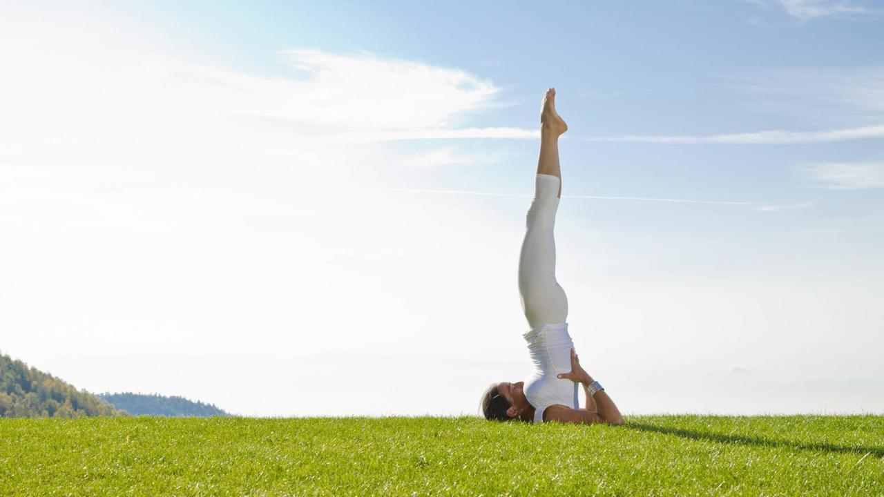 Eine junge Frau praktiziert Hatha-Yoga und zeigt den Schulterstand (Sarvangasana, auch Kerze genannt). Eine junge Frau praktiziert Hatha-Yoga und zeigt den Schulterstand (Sarvangasana, auch Kerze genannt).