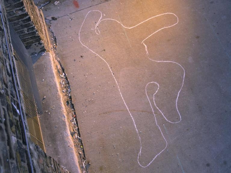 Im schummrigen Licht einer Straßenlaterne ist ein mit Kreide gezeichneter Umriss eines Menschen zu erkennen.