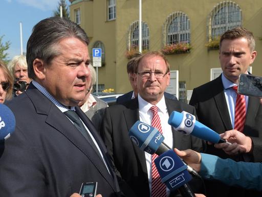 Gabriel, Opitz und der sächsische Wirtschaftsminister Dulig sprechen in Mikrofone und sind von Journalisten umringt.