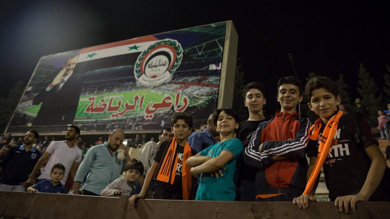 Jungen posieren vor einer Werbetafel mit dem syrischen Präsidenten Bashar al Assad beim Finale des syrischen Fußballpokals im Tishreen-Stadion. 