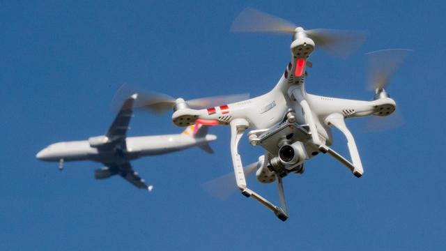 Das Foto zeigt eine private Drohne, dahinter in weiter Entfernung ein Flugzeug im Anflug auf den Flughafen Düsseldorf.
