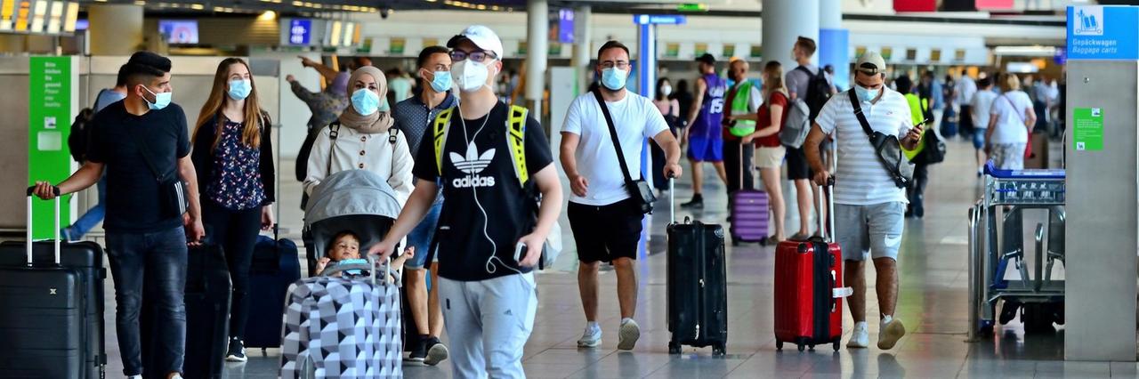 Reisende am Flughafen Frankfurt, im Hintergrund ist ein Schild zu sehen mit der Aufschrift "Covid-19-Test". Reisende am Flughafen Frankfurt, im Hintergrund ist ein Schild zu sehen mit der Aufschrift "Covid-19-Test".