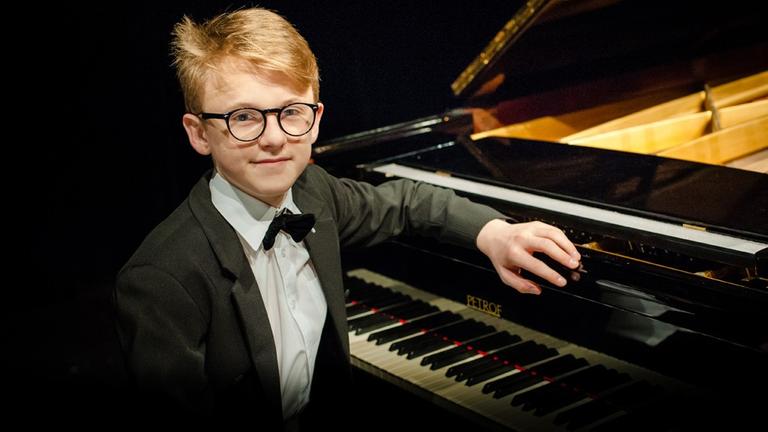 Der 16-Jährige sitzt mit seiner auffällig schwarz gerandeten Brille am Klavier