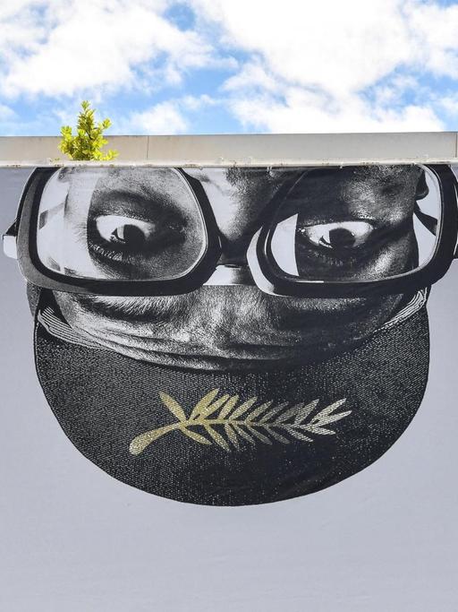 Ein riesiges Banner der 74. Filmfestspiele von Cannes, mit der Darstellung eines umgedrehten, männlichen Kopfes mit Brille und dem Logo der Filmfestspiele.