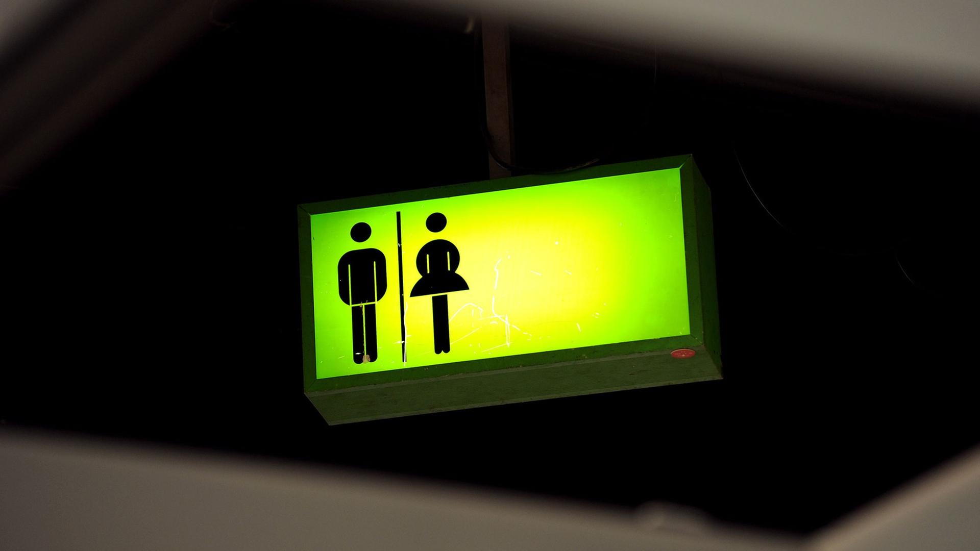 Ein grün leuchtendes Toiletten-Hinweisschild hängt auf dem Messegelände in Frankfurt am Main unter der Decke Ein grün leuchtendes Toiletten-Hinweisschild hängt auf dem Messegelände in Frankfurt am Main unter der Decke