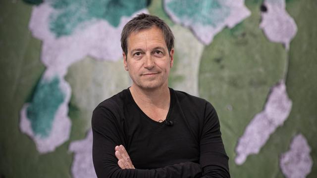 Porträt von Dieter Nuhr mit verschränkten Arnmen vor einem Kunstwerk