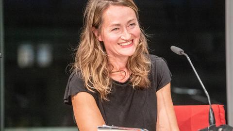 Katerina Poladjan lächelt bei einer Lesung von "Hier sind Löwen" in der Berliner Akademie der Künste ins Publikum. Sie trägt ein dunkles T-Shirt, vor ihr steht ein Mikrofon.