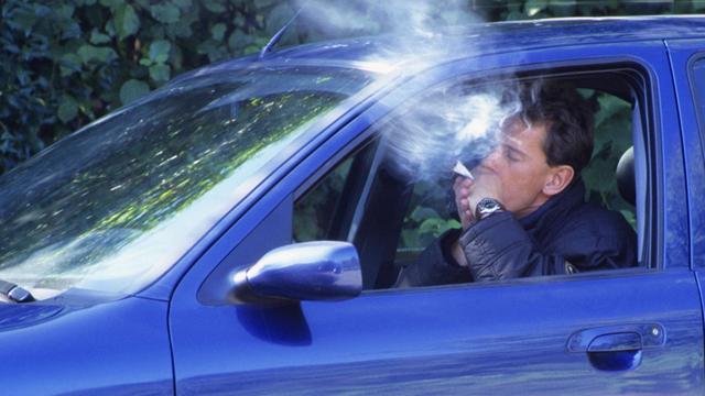 Ein Autofahrer raucht einen Joint am Steuer. Rauch quillt aus dem Fenster. Das Auto ist blau.
