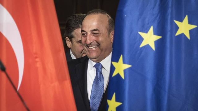 Zwischen der türkischen und der europäischen Flagge lächelt der Außenminister der Türkei Mevluet Cavusoglu, aufgenommen bei einem Besuch in der Villa Borsig in Berlin am 06.03.2018.