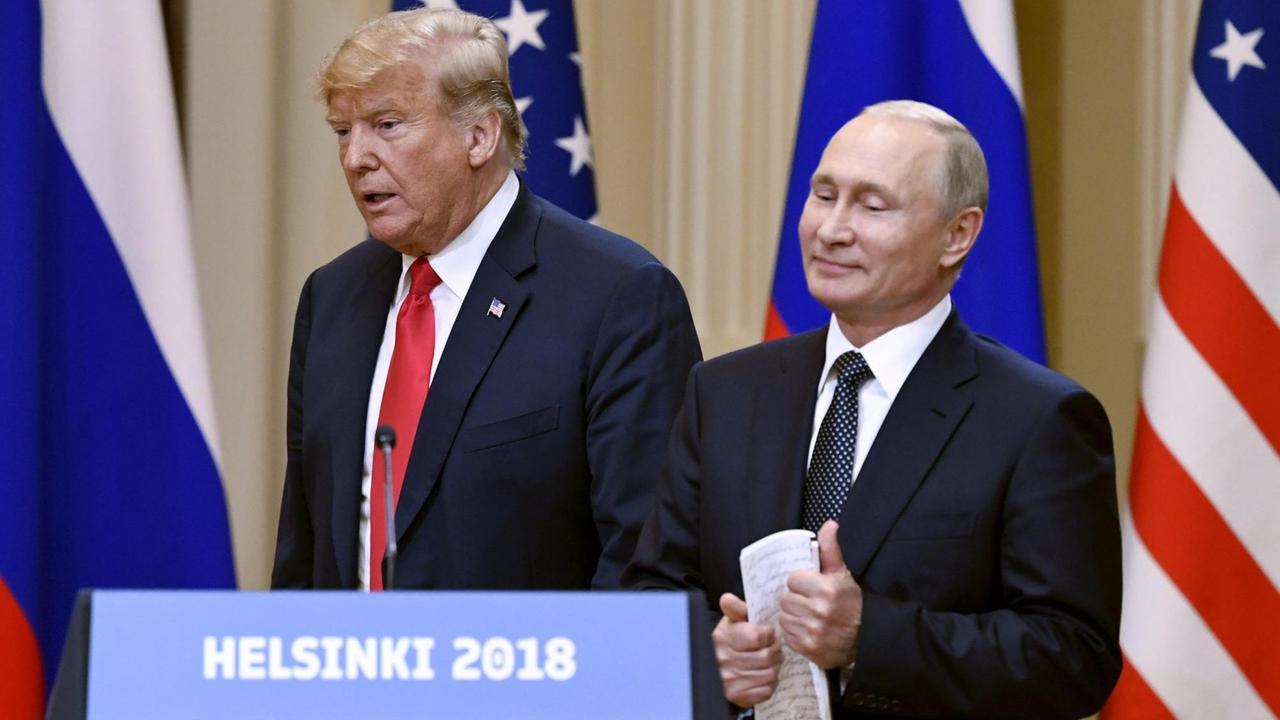 Trump sagt etwas, Putin steht lächelnd daneben. Vor ihnen ein Schild mit der Aufschrift "Helsinki 2018", hinter ihnen die Fahnen beider Staaten. Trump sagt etwas, Putin steht lächelnd daneben. Vor ihnen ein Schild mit der Aufschrift "Helsinki 2018", hinter ihnen die Fahnen beider Staaten.