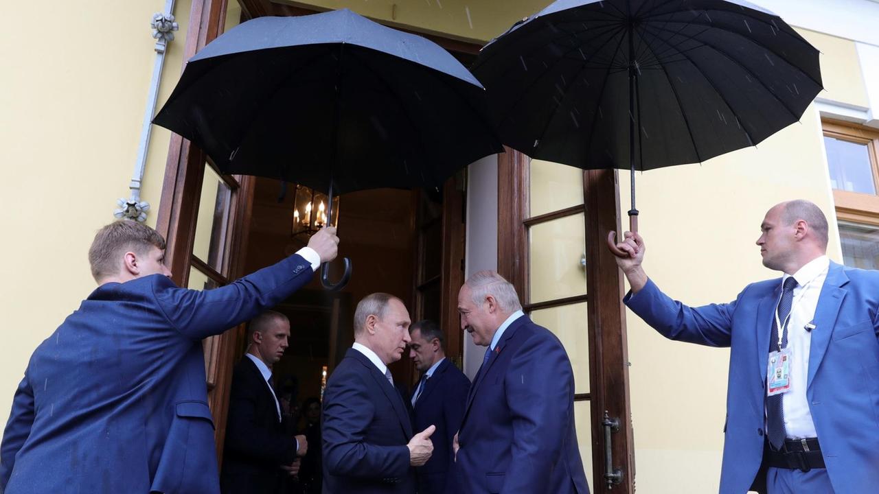 Der russische Präsident Wladimir Putin verabschiedet - unterm Schutz von blauen Regenschirmen - den weißrussischen Präsidenten Alexander Lukaschenko nach gemeinsamen Gesprächen am 18. Juli 2019 in Sankt Petersburg.
