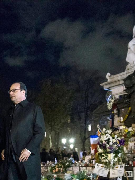 Bundeskanzlerin Merkel und Frankreichs Präsident Hollande auf der Place de la République in Paris, es ist dunkel, beide tragen Mäntel.