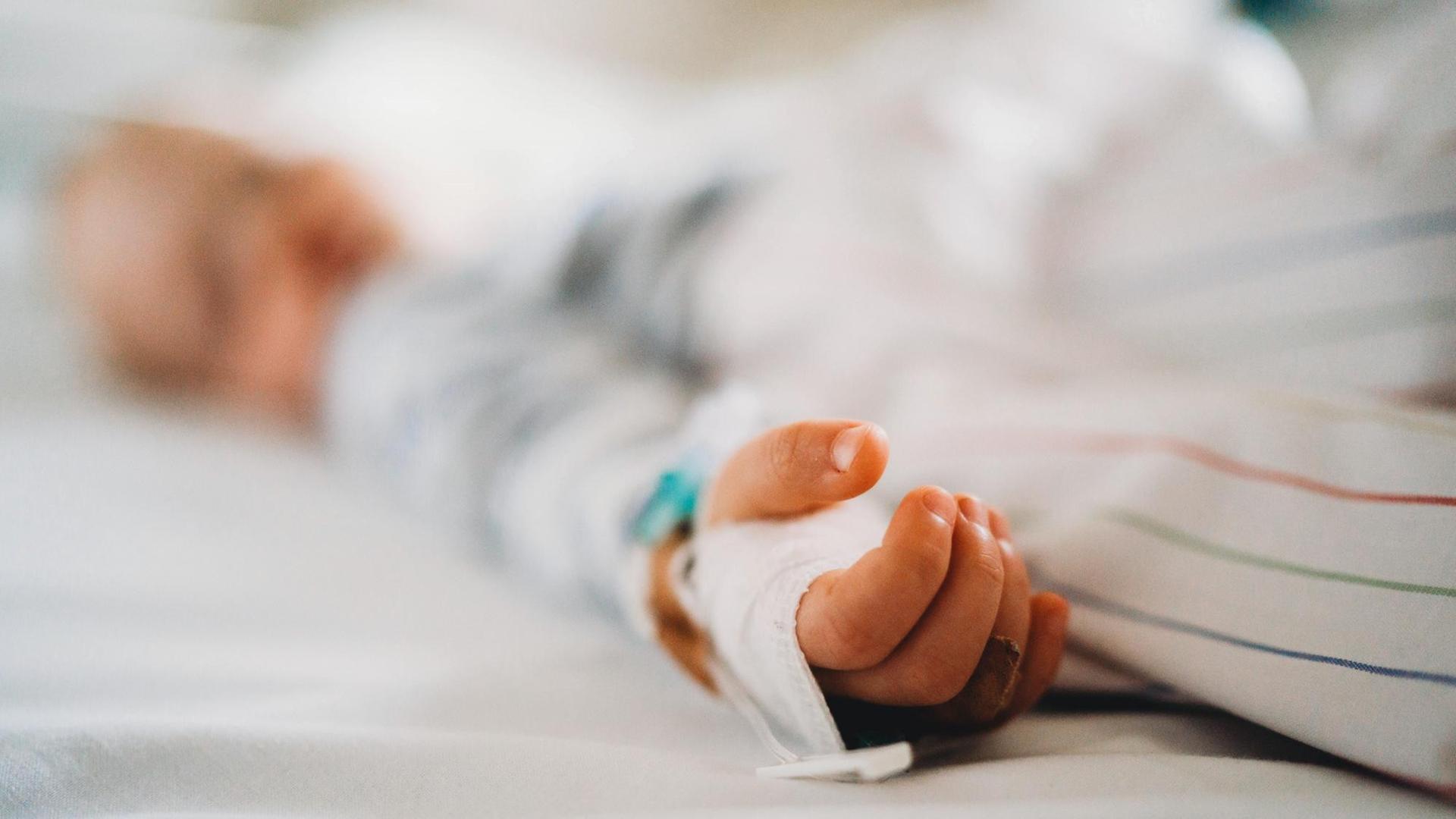 Aufnahme eines Kindes im Krankenhausbett, die Schärfe liegt auf der Hand des Kindes.