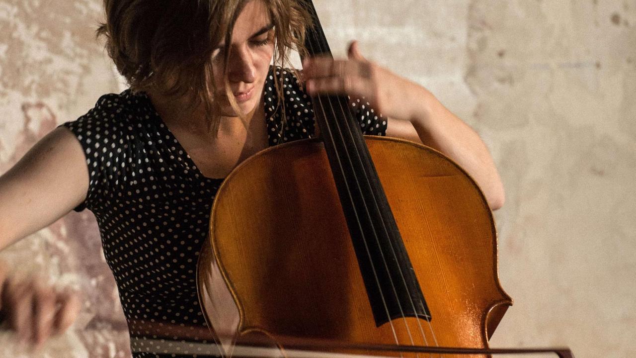 Eine junge Frau mit braunem, schulterlangem Haar spielt mit schnellen Bewegungen Violoncello. Eine junge Frau mit braunem, schulterlangem Haar spielt mit schnellen Bewegungen Violoncello.