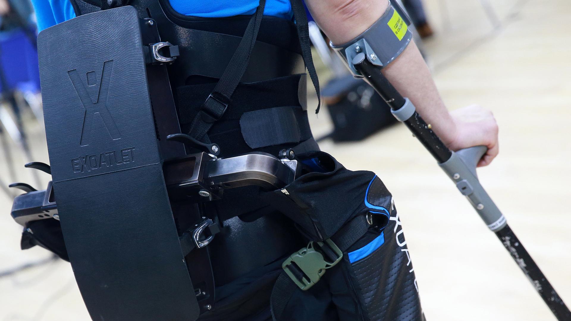 Ein Mann läuft mit einer technischen Apparatur am Körper und mit Krücken. Ein Mann läuft mit einer technischen Apparatur am Körper und mit Krücken.