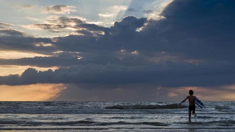 Ein Kind mit Surfbrett läuft im Abendlicht in die Wellen am Strand von St Peter-Ording, Nordfriesland, Schleswig-Holstein. Ein Kind mit Surfbrett läuft im Abendlicht in die Wellen am Strand von St Peter-Ording, Nordfriesland, Schleswig-Holstein.
