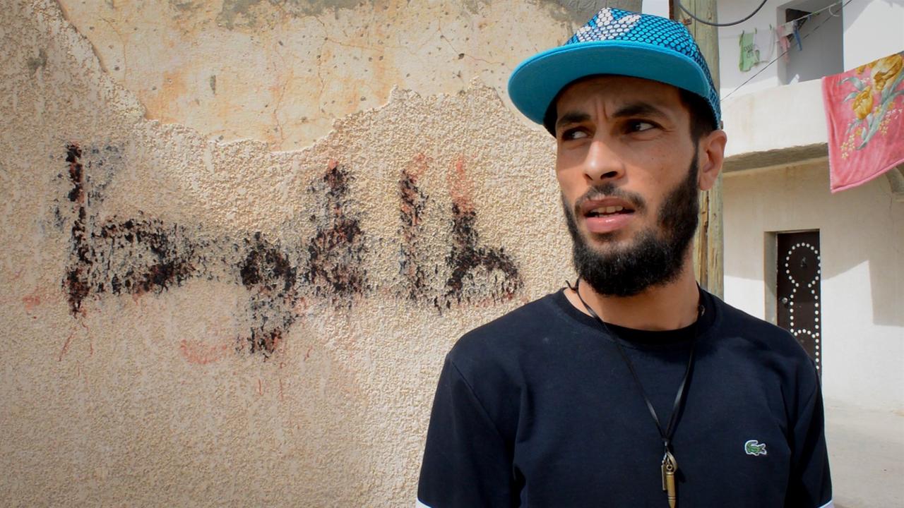 Mohamed Gladiateur steht vor einer Häuserwand.