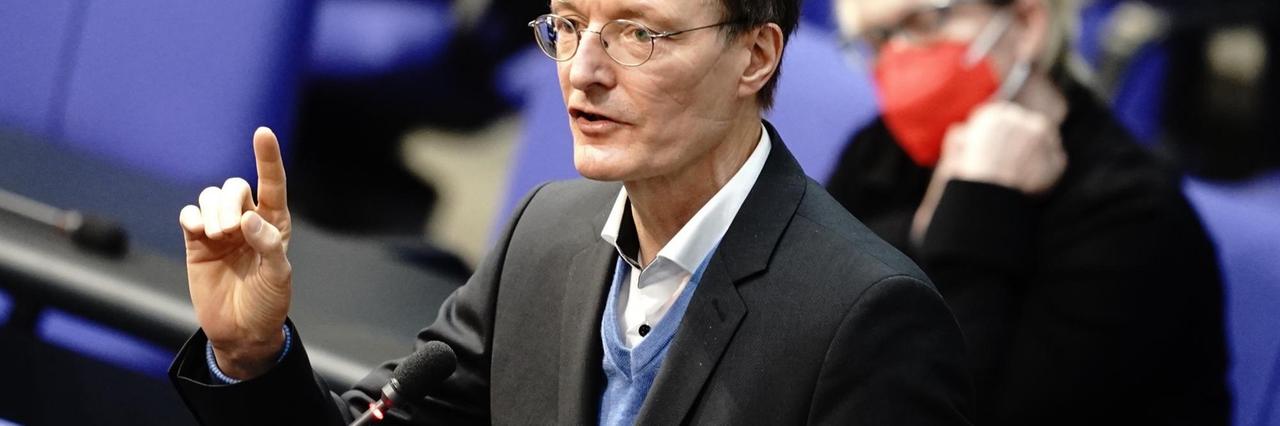 Karl Lauterbach steht im Bundestag und hebt die Hand. Karl Lauterbach steht im Bundestag und hebt die Hand.
