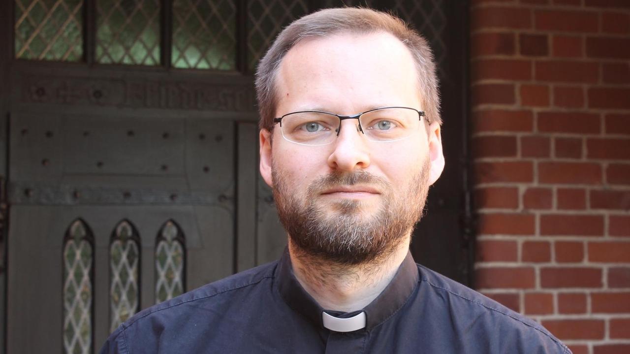 Thomas Kaiser, mit Vollbart und Brille, in schwarzer Robe, steht vor einer Wand aus roten Ziegeln Thomas Kaiser, mit Vollbart und Brille, in schwarzer Robe, steht vor einer Wand aus roten Ziegeln