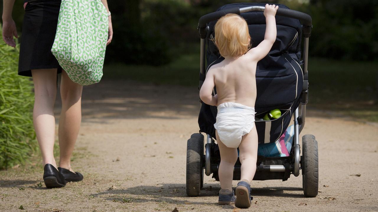 Nur mit einer Windel bekleidet, schiebt der knapp zweijährige Junge den Kinderwagen durch einen Park. Nur mit einer Windel bekleidet, schiebt der knapp zweijährige Junge den Kinderwagen durch einen Park.