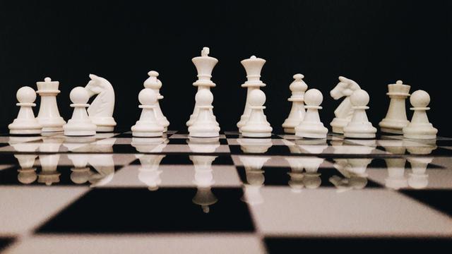 Weiße Schachfiguren stehen vor schwarzem Hintergrund auf einem Schachbrett.