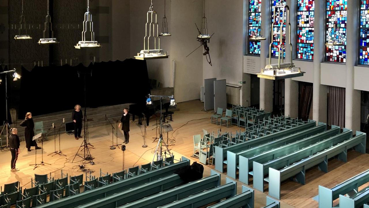 Blick von der Orgelempore in den Kirchenraum mit leeren Kirchenbänken und probenden Sängerinnen.