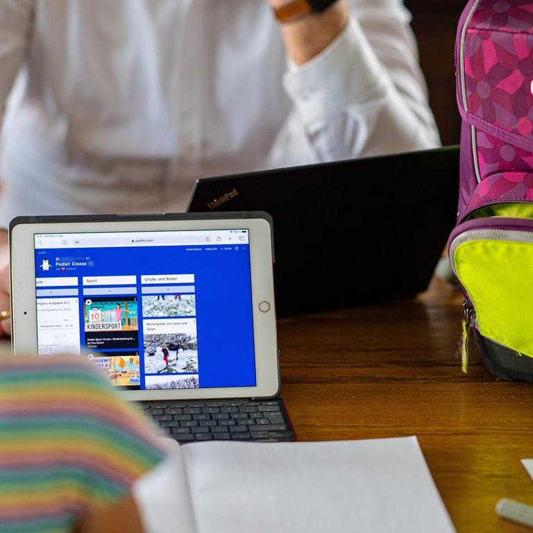 Eine siebenjährige Erstklässlerin sitzt vor einem iPad, welches eine "Padlet Klasse 1b" darstellt und lernt im Homeschooling für die Schule. 