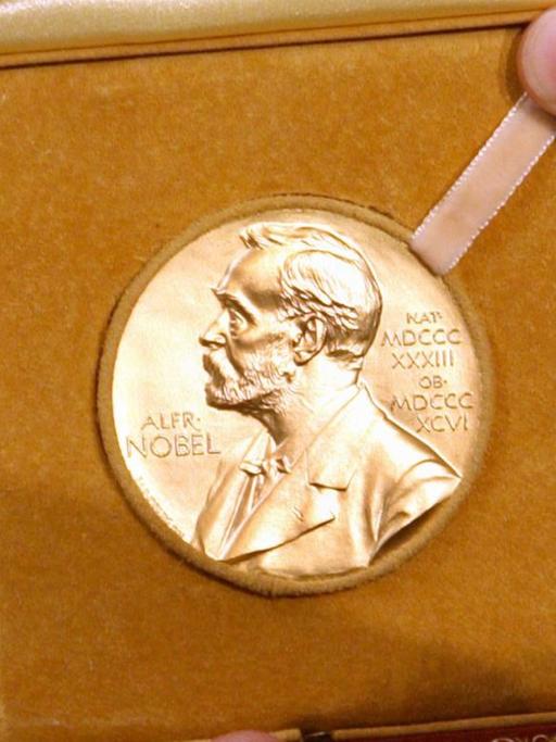 Mehrere Hände halten die Medaille mit dem Konterfei von Alfred Nobel